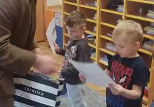 Pan leśnik stoi przezd chłopcem. Trzyma w ręku torbę prezentową. Wręcza mu dyplom.