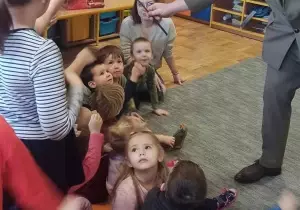 Pan leśnik wyciąga gałązkę wiesiołka do dzieci. Pokazuje wygryzione miejsca przez ptaki.