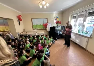 Dzieci siedzą na podłodze w Domu Dziennego Pobytu Senior Vigor. Przed nimi stoi pan. Opowiada im o swoich zdolnościach.