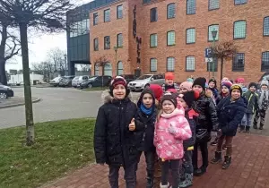 Dzieci ubrane są w kurtki i czapki. Stoją przed budynkiem Starego Młyna w Zgierzu.