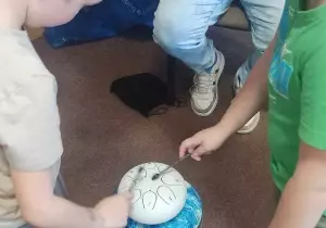 Dw&oacute;ch chłopc&oacute;w stoi przy instrumencie. Grają na nim pałeczkami.