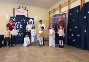 Dzieci uczestniczące w konkursie stoją ze swoimi nauczycielami. Z tyułu jest dekoracja co nam powie pani zima