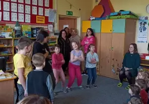 Na środku stoją trzy dziewczynki. Obok stoi Pani od hip hopu. Razem tańczą