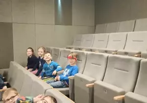 Dzieci siedzą w kinie na fotelach.
