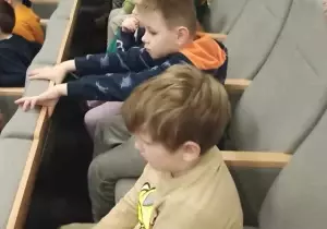 Dzieci siedzą w kinie na fotelach.