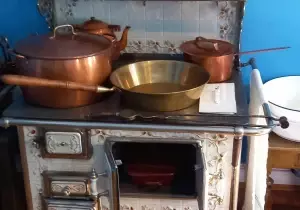 Na zdjęciu znajduje się starodawny piec. Na nim stoi patelnie, garnki, czajnik.