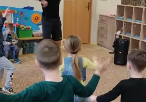 Dzieci tańczą w sali przedszkolnej. Przed nimi stoi pan Bartłomiej instruktor tańca.