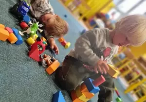 dzieci siedzą na dywanie i bawią się klockami
