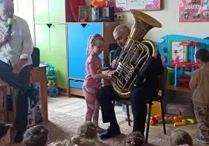 Pan gra na tubie. Dziewczynka stoi obok. Naciska klawisze.
