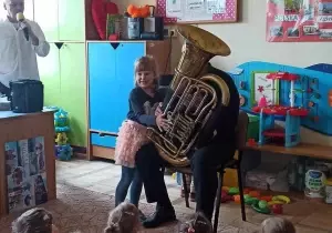 Pan gra na tubie. Dziewczynka stoi obok. Naciska klawisze.