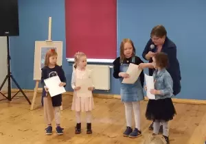 Julia otrzymuje dyplom od Pani prowadzącej. Obok niej stoją trzy laureatki.