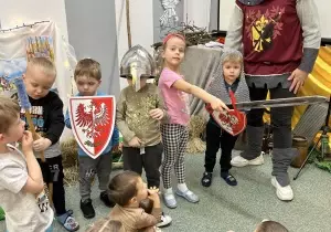 Dzieci trzymają tarcze i miecze. Pozują do zdjęcia. Uśmiechają się.
