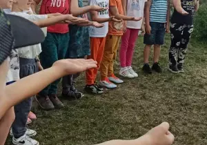 Dzieci wyciągają ręce do przodu. Stoją jeden obok drugiego.