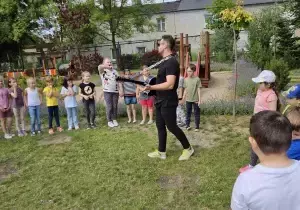 dzieci stoją w kole, nauczyciel gra na gitarze