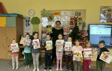 Nauczycielka stoi z dziećmi w grupie. Uśmiechają się do zdjęcia. Trzymają w rękach książki.