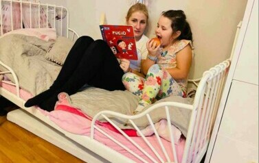 Mama czyta c&oacute;rce książkę. Leżą na ł&oacute;żeczku.