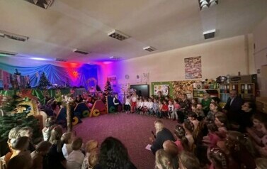 Na zdjęciu pokazana jest cała scena teatralna. Kolorowa dekoracja, pociąg. Na widowni siedzą goście. Aktorzy stoją na scenie.