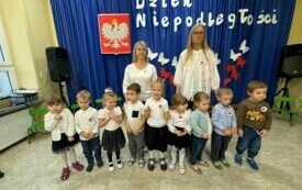 Dzieci stoją wraz z nauczycielem przed dekoracją .