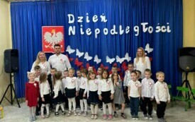 Dzieci stoją wraz z nauczycielem przed dekoracją .