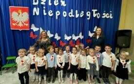Dzieci stoją wraz z nauczycielem przed dekoracją .