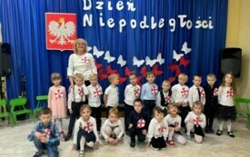 Dzieci stoją wraz z nauczycielem przed dekoracją .