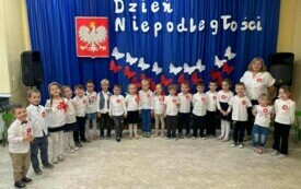 Dzieci stoją wraz z nauczycielem przed dekoracją .