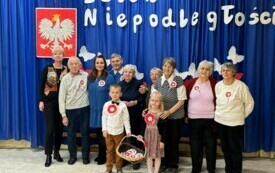 Dzieci stoją wraz z zaproszonymi gośćmi przed dekoracją .