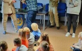 Rycerz prezentuje cały str&oacute;j ,dzieci siedzą i oglądają  z zaciekawieniem.  