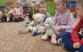 Dzieci siedzą na dywanie. Trzymają w rękach misie.