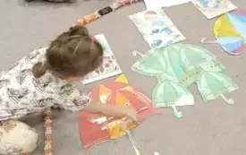 Dziewczynka kładzie na dywanie czerwoną parasolkę wyciętą z papieru.