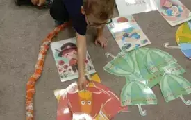 Chłopiec kładzie na dywanie czerwoną parasolkę wyciętą z papieru.