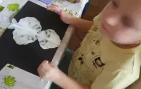 Chłopiec siedzi przy stoliku. Przed nim leży kartka z odciśniętym wzorem.