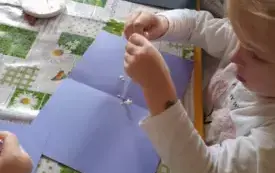 Dziewczynka siedzi przy stoliku. Naciska pipetę. Z pipety wypływa płyn na fioletową kartkę.