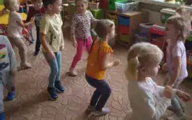Dzieci stoją w rozsypce na dywanie w przedszkolu.