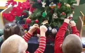 Dzieci wieszają bombki na choince.