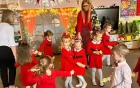 Dziewczynki przebrane w czerwone sukienki tańczą. Razem z nimi tańczy nauczycielka.