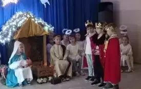 Dzieci przebrane za trzech kr&oacute;li stoją przy żł&oacute;bku. Przy żł&oacute;bku siedzi dziewczynka przebrana za Maryję i chłopiec przebrany za J&oacute;zefa. 