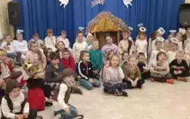 Zdjęcie grupowe dzieci z przedszkola oraz dzieci ze Szkoły Podstawowej numer 1 ze Zgierza. Za nimi stoi żł&oacute;bek i dekoracaja z białymi aniołami.