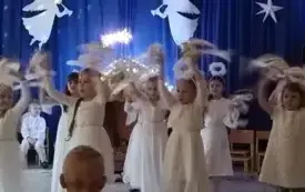 Dziewczynki przebrane za aniołki stoją na środku sali. Ubrane są w białe sukienki. Nad głowami mają aureole. Rękami machają nad głowami. W rękach mają białe i złote wstążeczki.