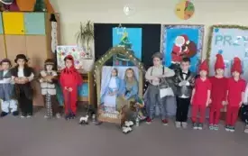 Dzieci stoją  przed dekoracją i uśmiechają się .