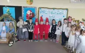 Dzieci stoją przed dekoracją w oczekiwaniu na rodzic&oacute;w,uśmiechają się. 