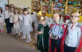 Dzieci stoją  przed dekoracją świąteczną i uśmiechają się .