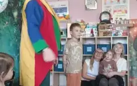 Iluzjo nista stoi na środku. Po jego prawej stronie stoi dziewczynka. Patrzy na niego. Po jego lewej stronie stoi chłopiec. Patrzy na dzieci siedzące przed nim.
