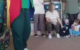 Iluzjonista stoi w sali przedszkolnej. Ubrany jest w czapkę z flagą Wielkiej Brytani i kolorowy frak.