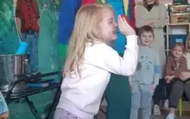 Dziewczynka stoi w sali przedszkolnej. Śmieje się. Obok niej stoi iluzjonista. Ubrany w czapkę z flagą Wielkiej Brytani i kolorowy frak. Z drugiej strony iluzjonisty stoi chłopiec. Patrzy.