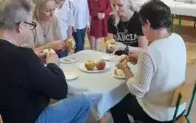 babcie i dziadkowie siedzą przy stoliku i obierają jabłko. 