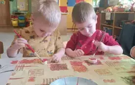 Chłopcy siedzą przy stoliku. Malują farbami serduszko wykonane z masy solnej.