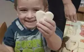 Chłopiec uśmiecha się. Pokazuje serduszko wykonane z masy solnej.