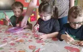 Dzieci siedzą przy stoliku. Bawią się masą solną. St&oacute;łprzykryty jest ceratą.
