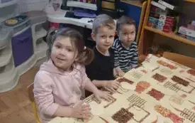 Dziewczynka i dw&oacute;ch chłopc&oacute;w siedzą przy stoliku. Na stoliku przed nimi leżą serduszka z masy solnej.